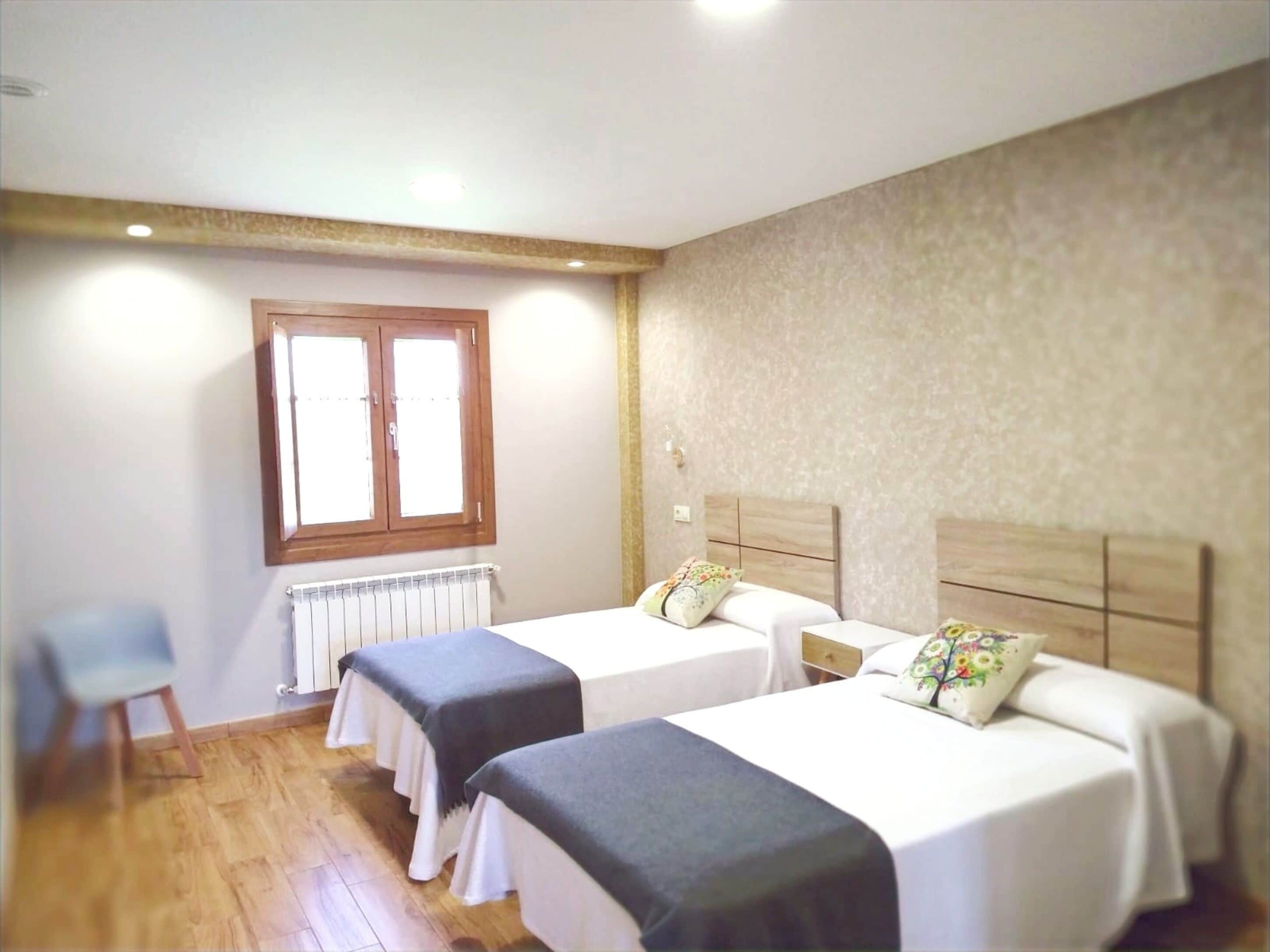 Ein Hotelzimmer mit zwei Betten, einem Fenster, einem Heizkörper und einem Stuhl.