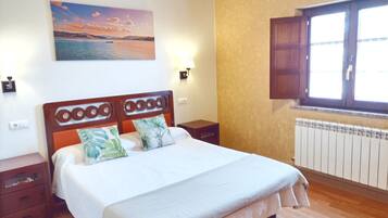 A bedroom with a wooden bed, a nightstand, a wall-mounted painting, a window with wooden shutters, and a radiator.