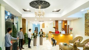 Un vestíbulo de hotel con mostrador de recepción, una araña de cristal y mobiliario de mimbre.