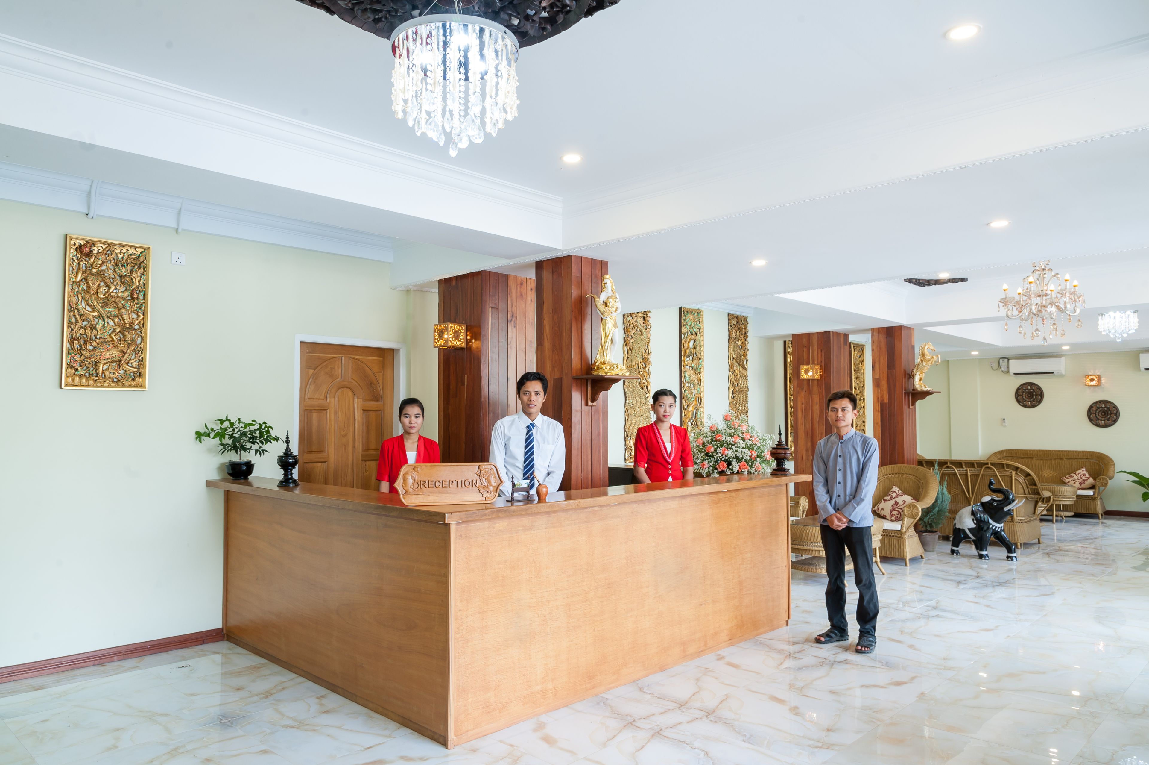 A reception desk with three staff members, a chandelier, and a reception area with a sofa and decorative items.