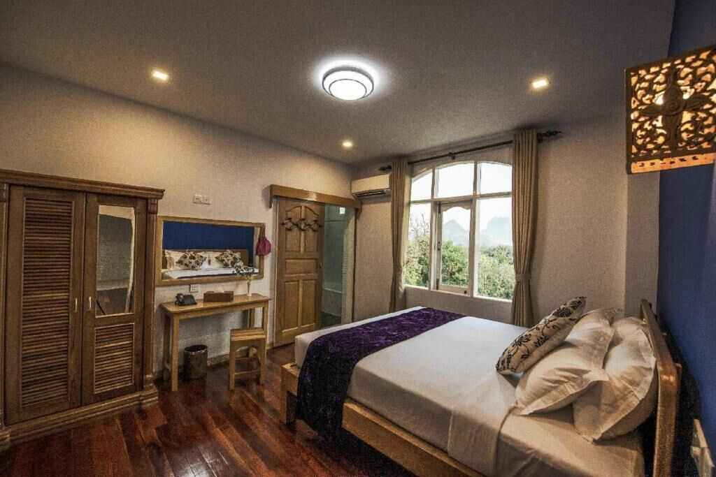 A bedroom with a bed, wooden wardrobe, desk, and a window with a view.