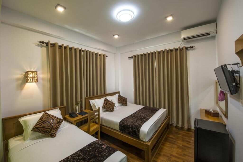 Habitación de hotel con dos camas, una mesita de noche con lámpara, aire acondicionado y televisor sobre un soporte.