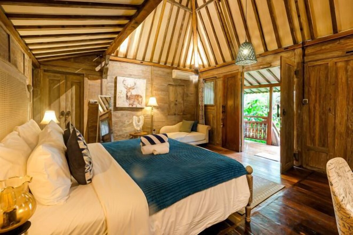 Quarto com cama, mesa de cabeceira, luminária e vista para o exterior.