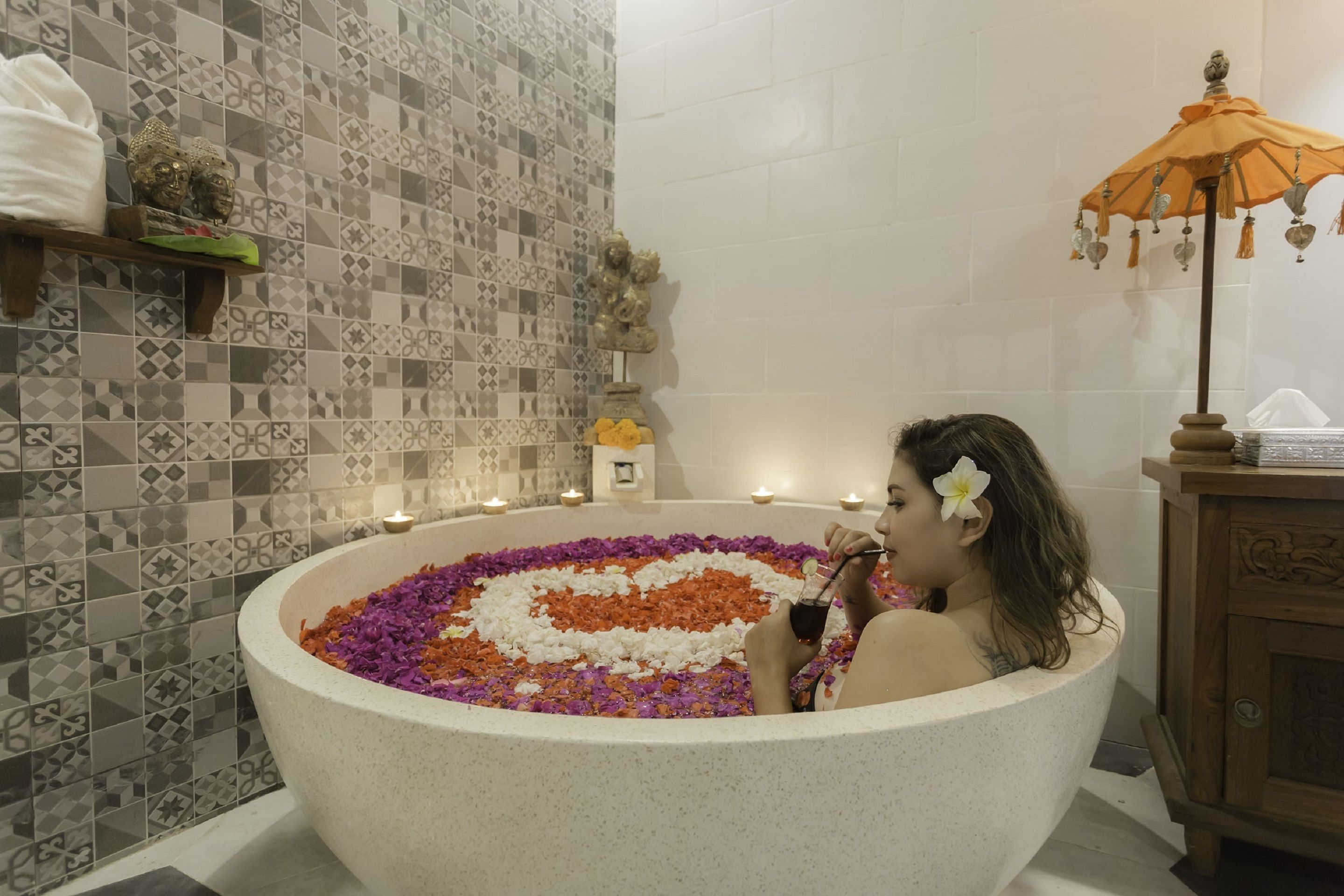 Una bañera llena de agua y pétalos de flores, rodeada por una pared de azulejos con un diseño geométrico.