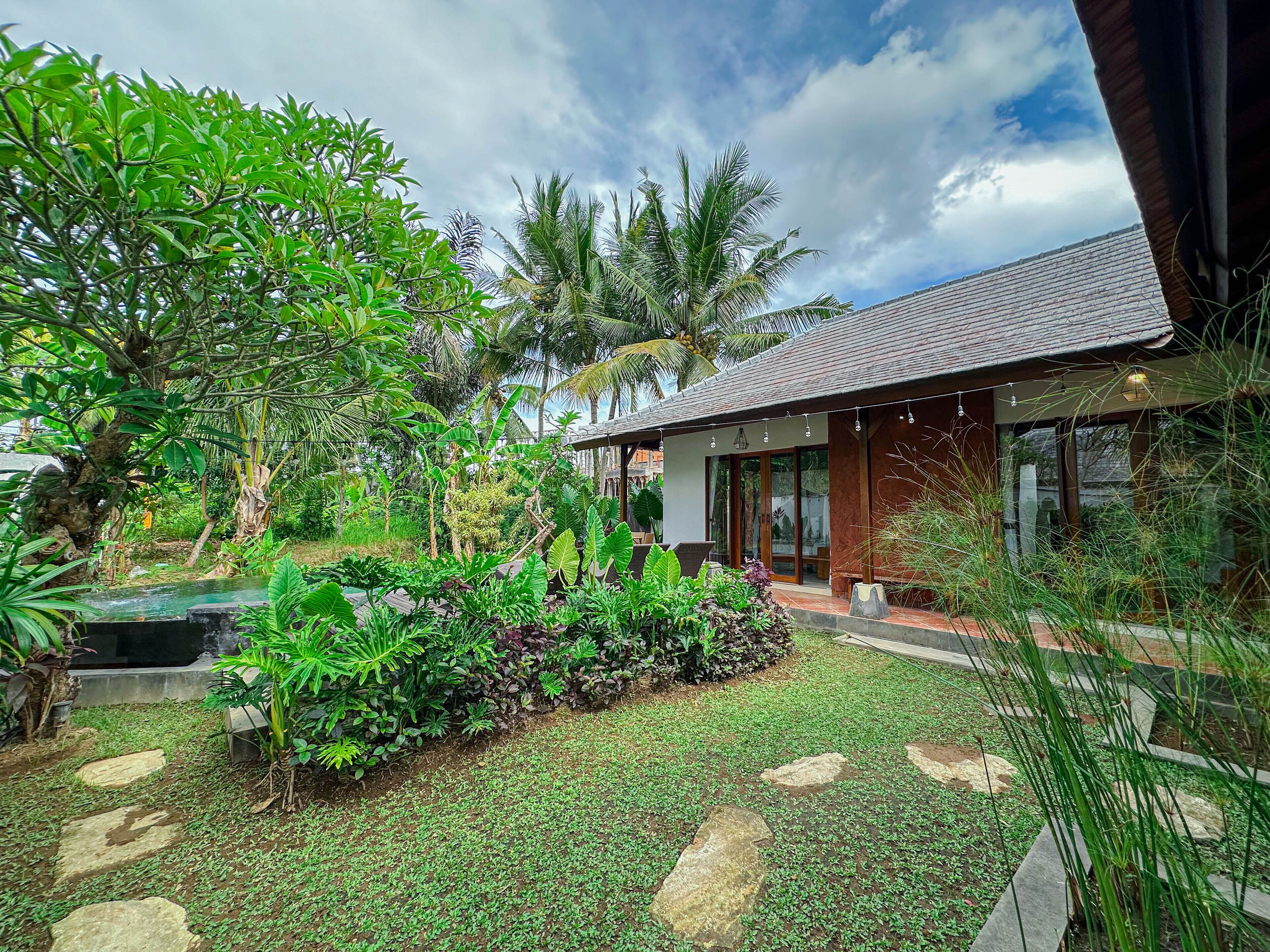 A modern house with a covered porch, surrounded by lush greenery and a small pond.