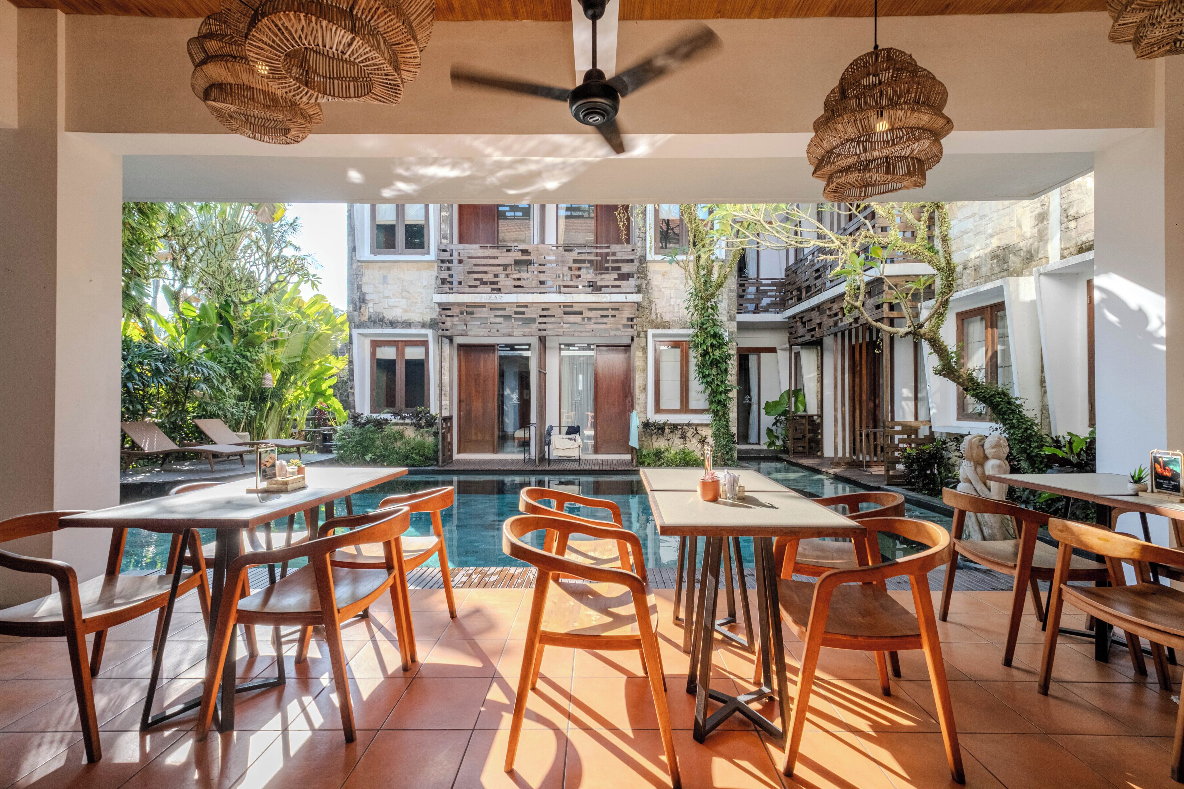 Un área de comedor al aire libre con piscina, muebles de madera y vista a un edificio con balcones.