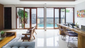 A spacious living area with a large sliding glass door leading to an outdoor pool area. - Kakul Villas & Suites (Ubud)
