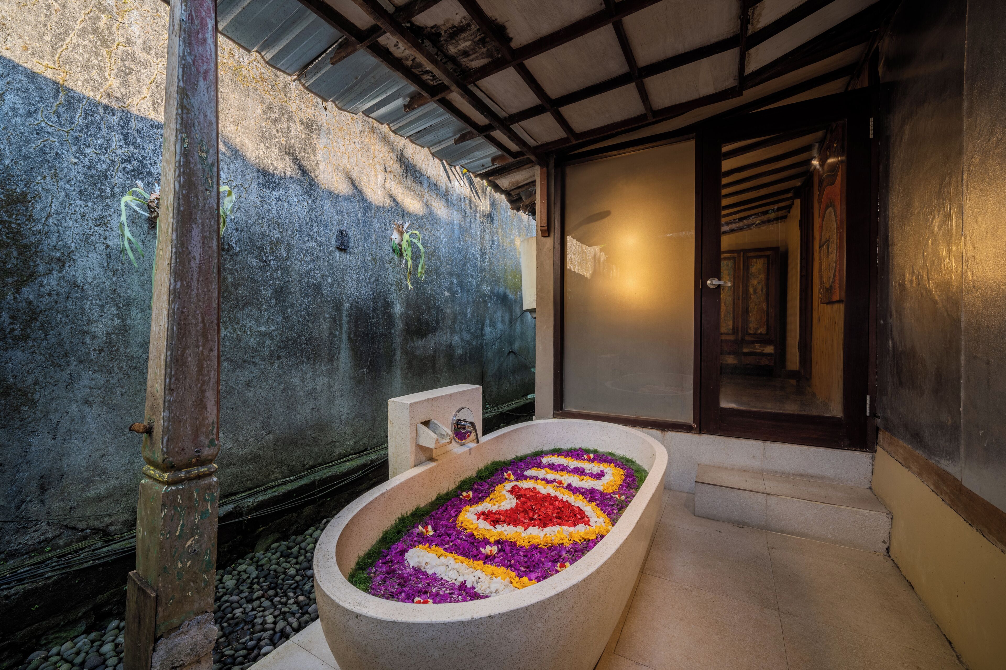 A bathroom with a flower arrangement in the tub, a concrete wall, and a wooden door.