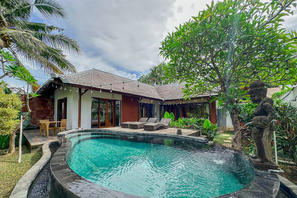 A house with a swimming pool, a patio with chairs, and a statue.