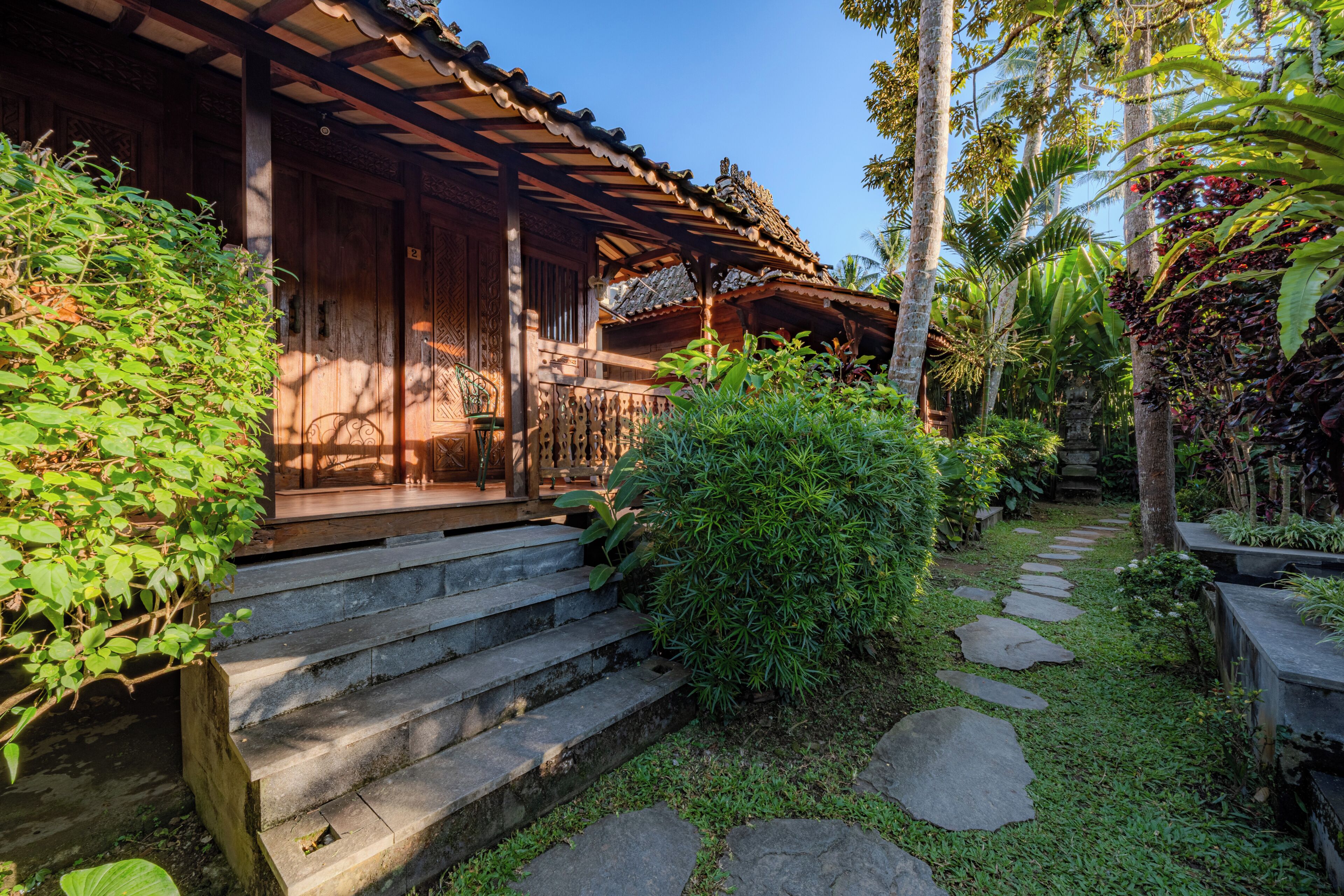 A traditional wooden building with a porch, stone steps, and a garden with tropical plants.