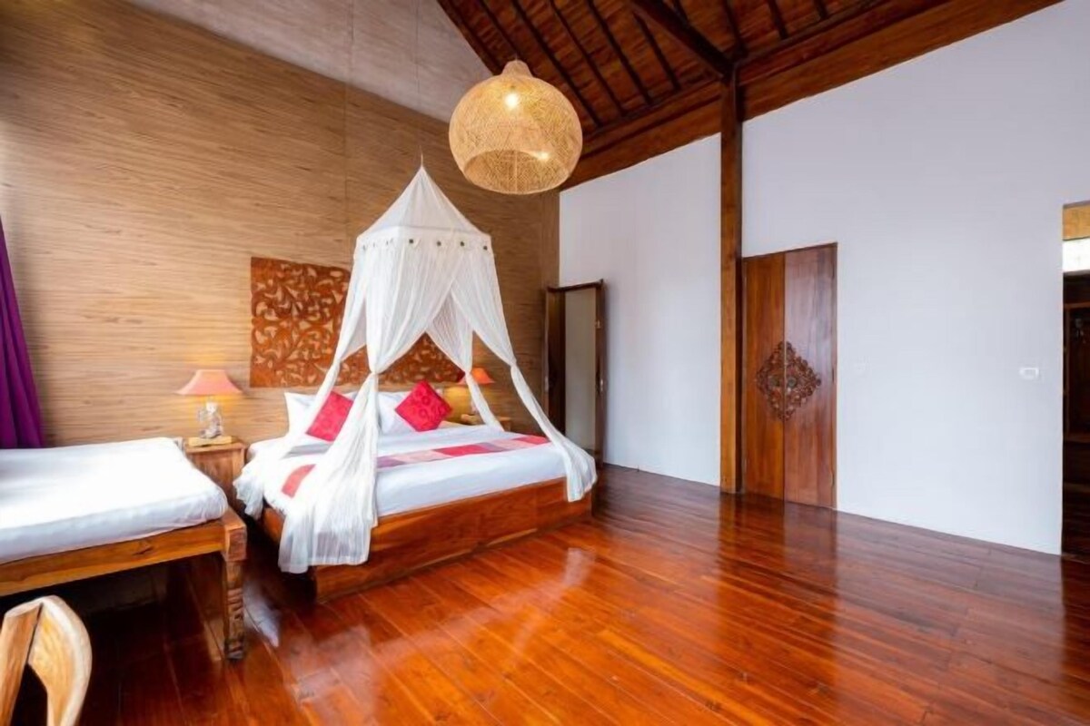 Un dormitorio con suelo de madera, cama con dosel, mesita de noche y lámpara.