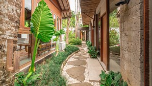A stone pathway leading to a wooden door, surrounded by lush greenery and a large leaf plant. - Kakul Villas & Suites (Ubud)