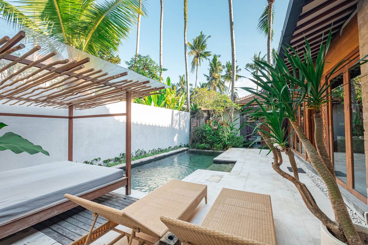 A poolside area with wicker furniture, a pergola, and tropical plants.