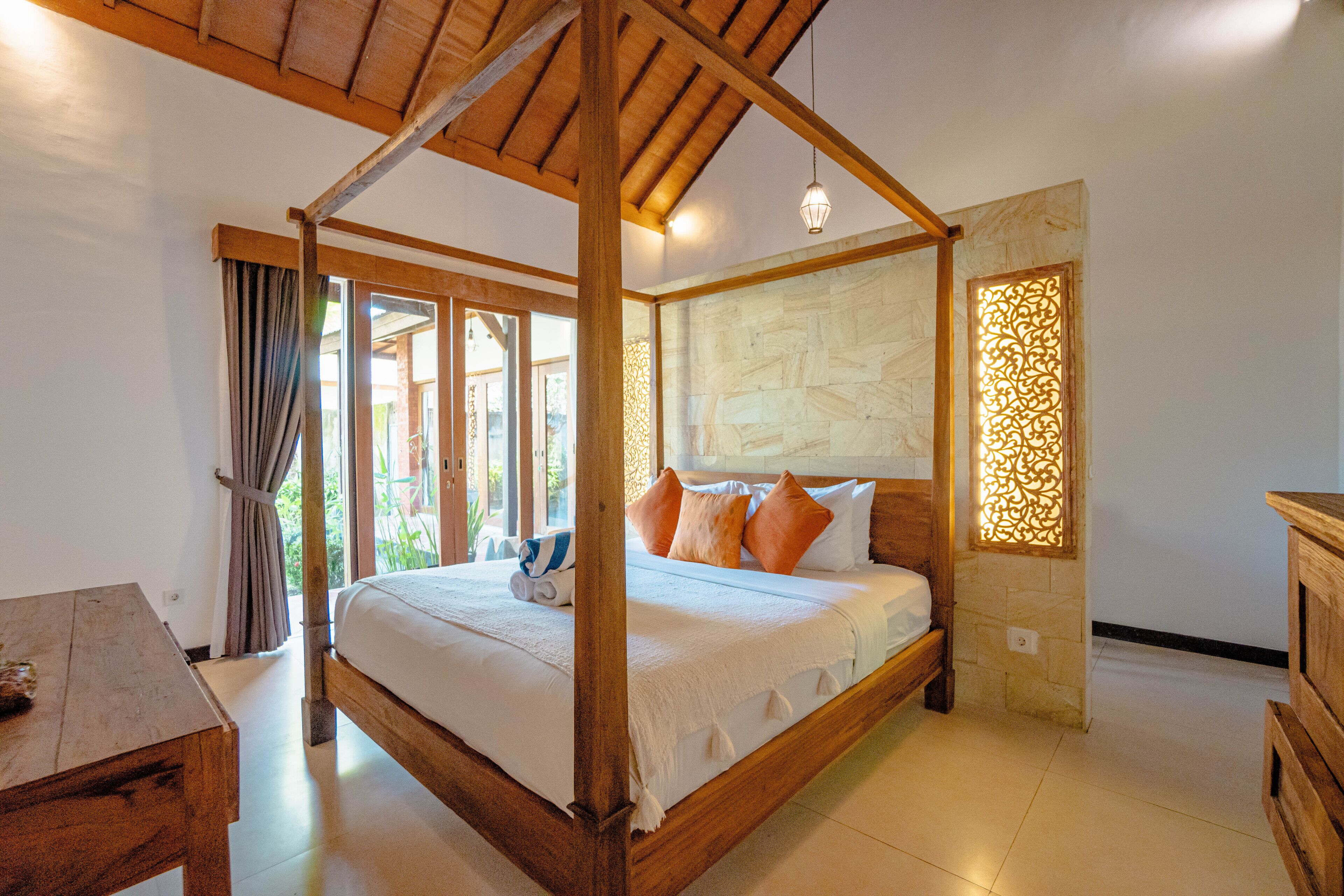 Una cama con dosel de madera, un ventanal con cortinas y una pared de piedra con un elemento decorativo de iluminación.