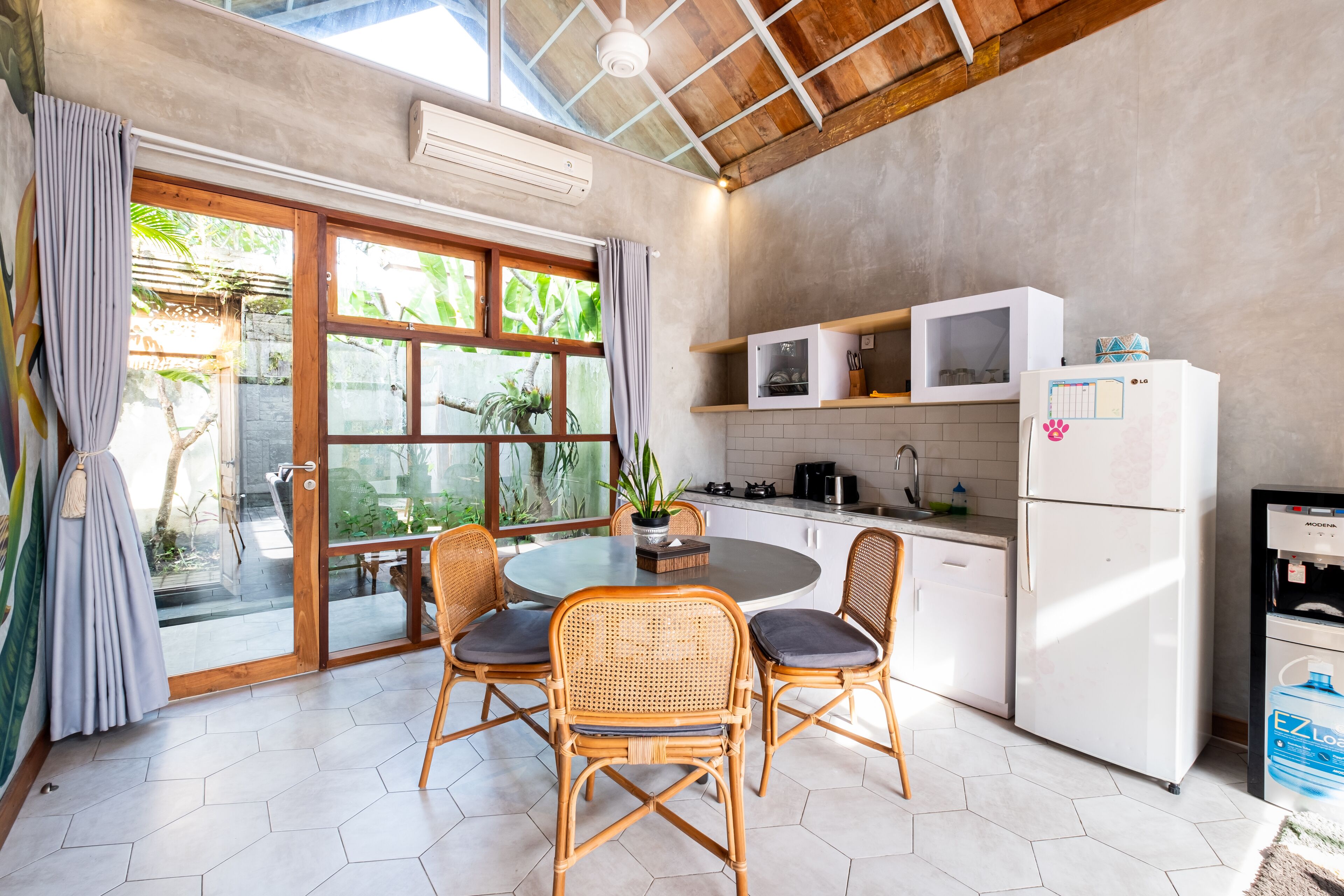 A kitchen with a round table, wicker chairs, a refrigerator, and a water dispenser.