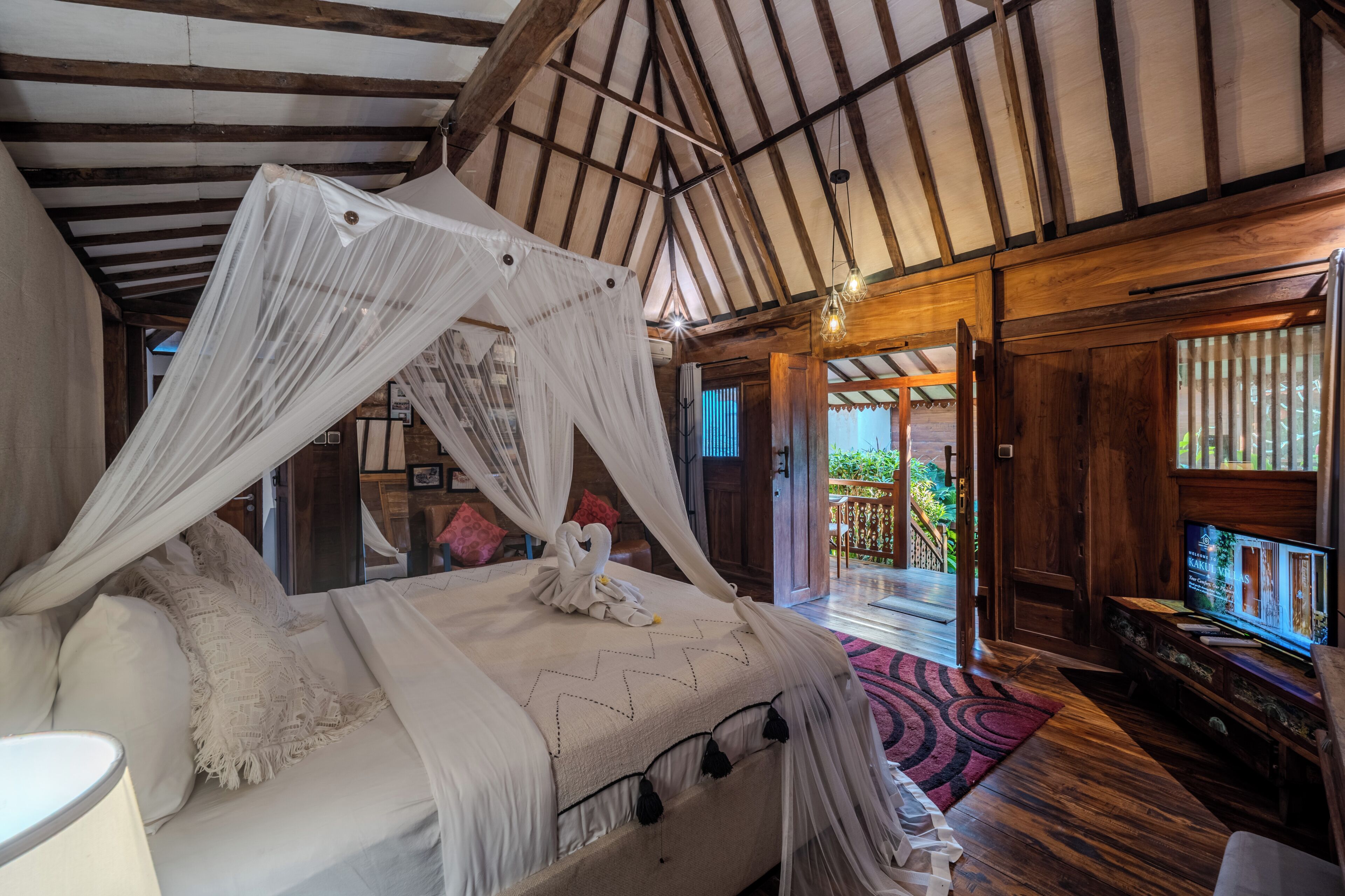 Ein Schlafzimmer mit Himmelsbett, Holzbalken, Fernseher und Blick ins Freie.