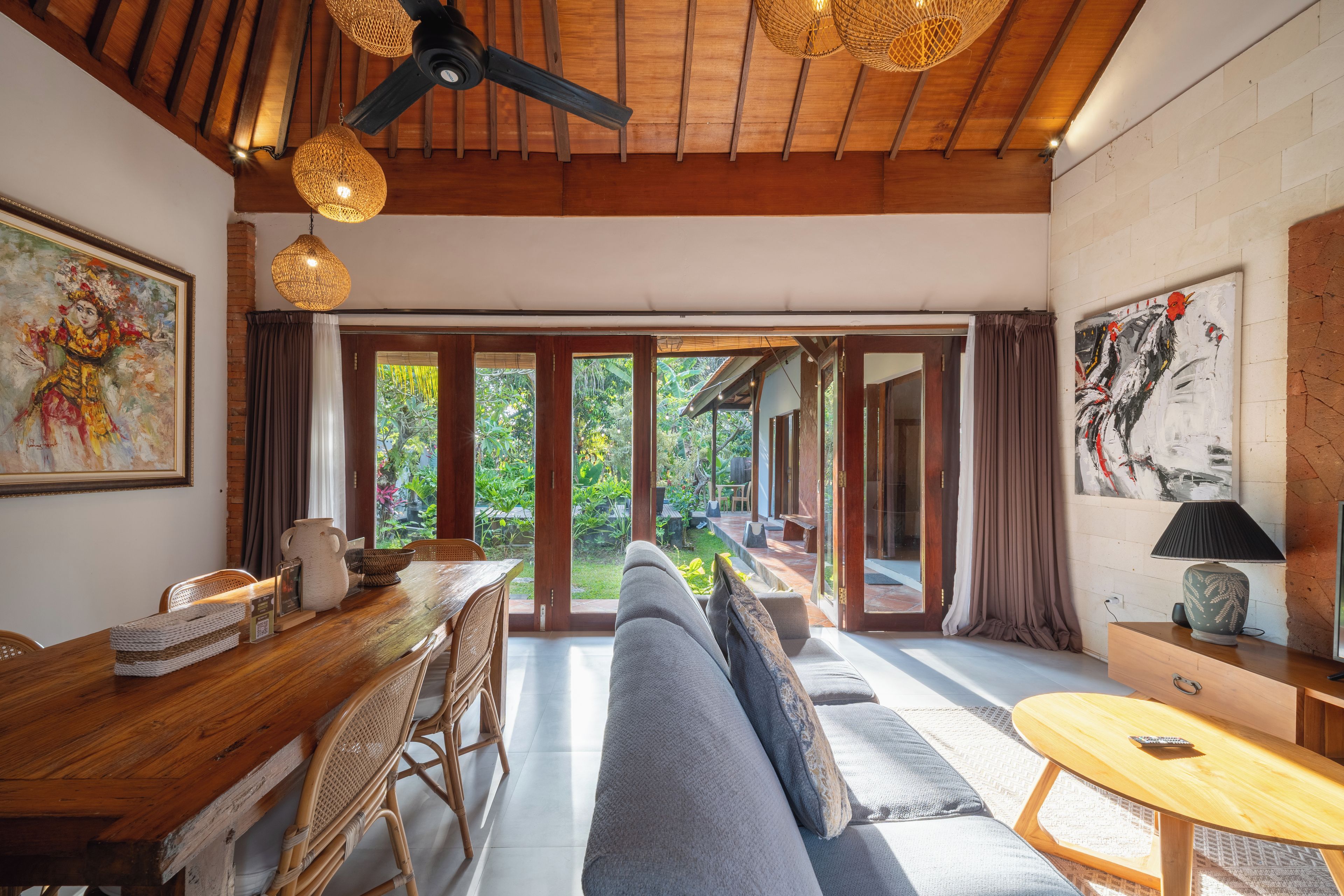 A spacious room with a large sliding glass door leading to a garden, a ceiling fan, and a dining area with a wooden table and chairs.