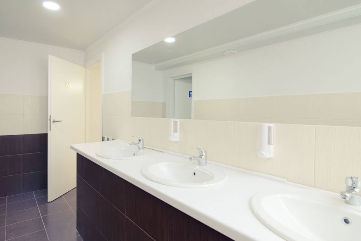 A modern bathroom with three sinks, a large mirror, and a door labeled "WC".