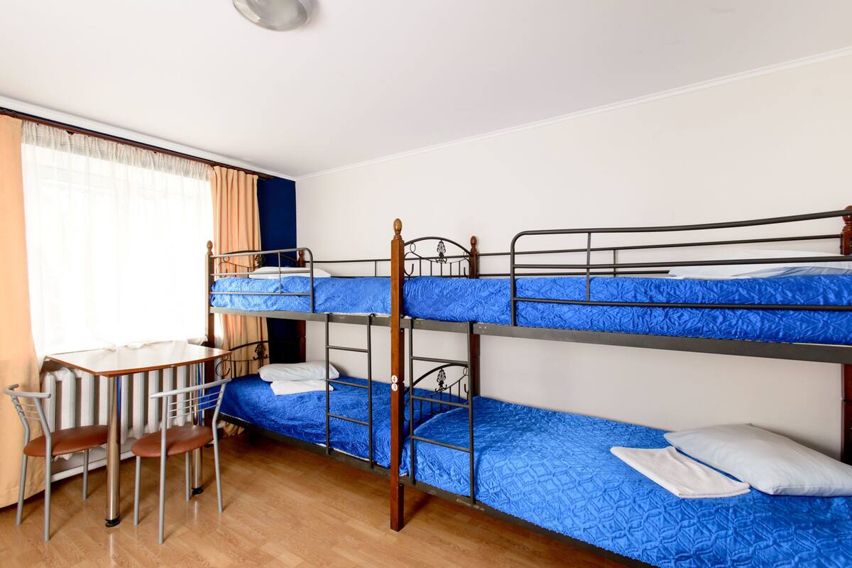 A bunk bed room with a desk and chair, a window with curtains, and a wooden floor.