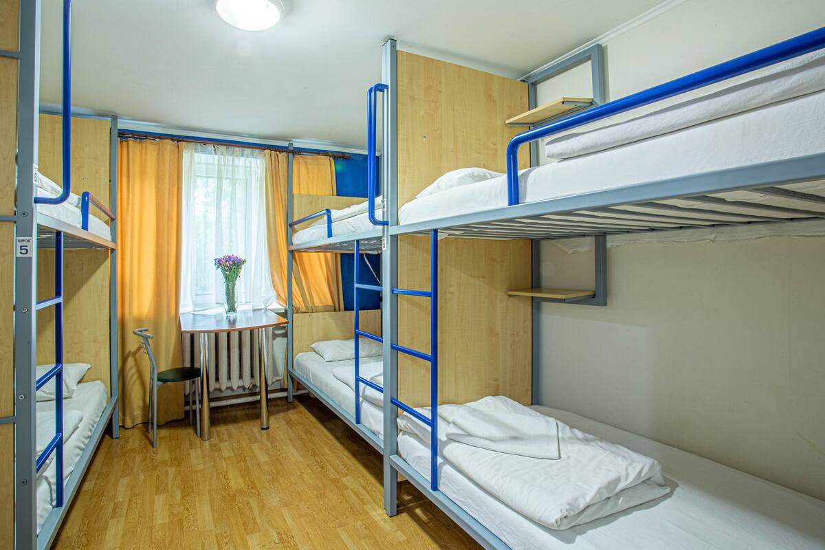 A bunk room with three bunk beds, a small table with a chair, and a window with curtains.