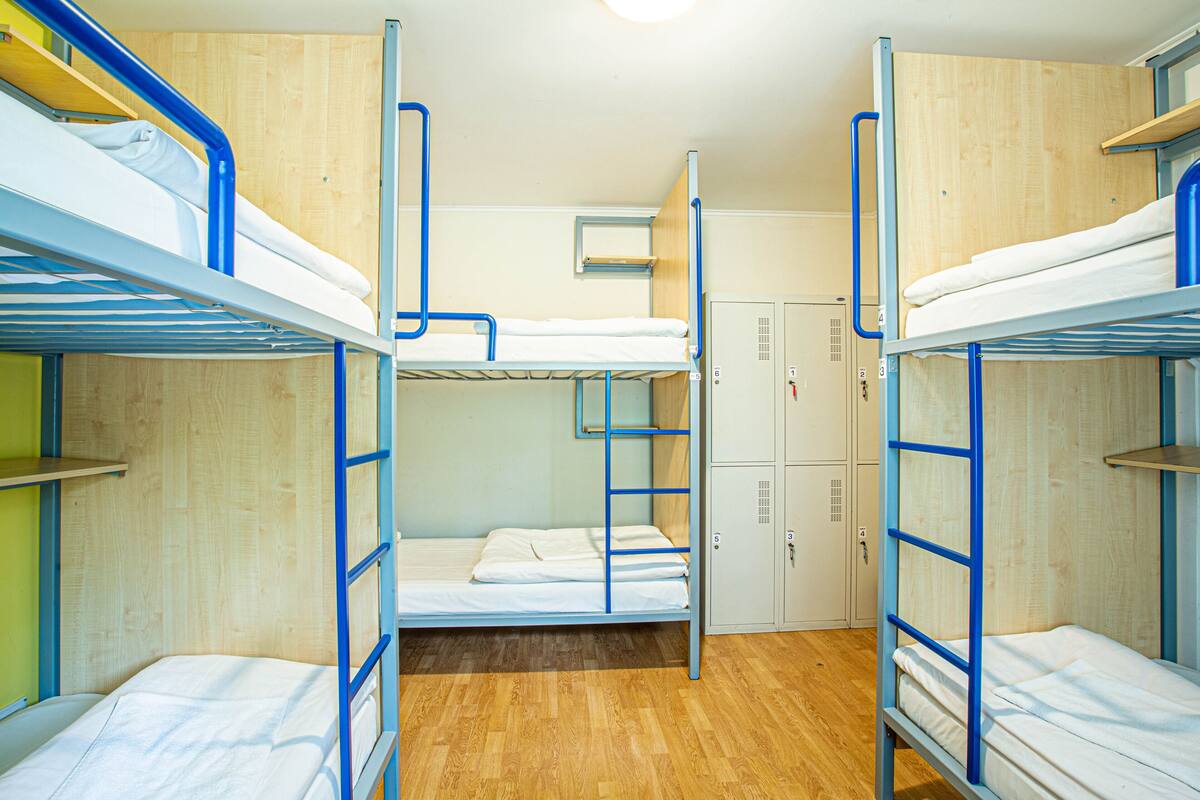 A dormitory room with bunk beds, wooden flooring, and a small window.