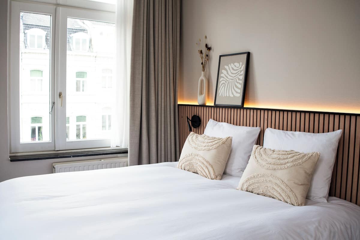 A hotel room with a large bed, a window with curtains, a wall-mounted light, and a framed picture.
