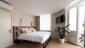 Une chambre à coucher moderne avec un lit, une plante en pot, un téléviseur et une fenêtre avec des rideaux.