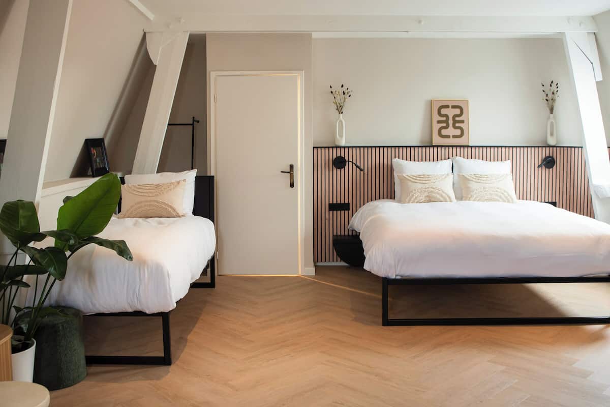 A modern bedroom with two beds, a wooden floor, and a sloped ceiling.