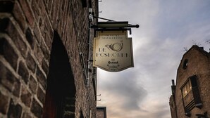 Une enseigne de pub portant le nom « De Poschorn » et la marque « Brand Pilsener », le tout sur fond de ciel nuageux.