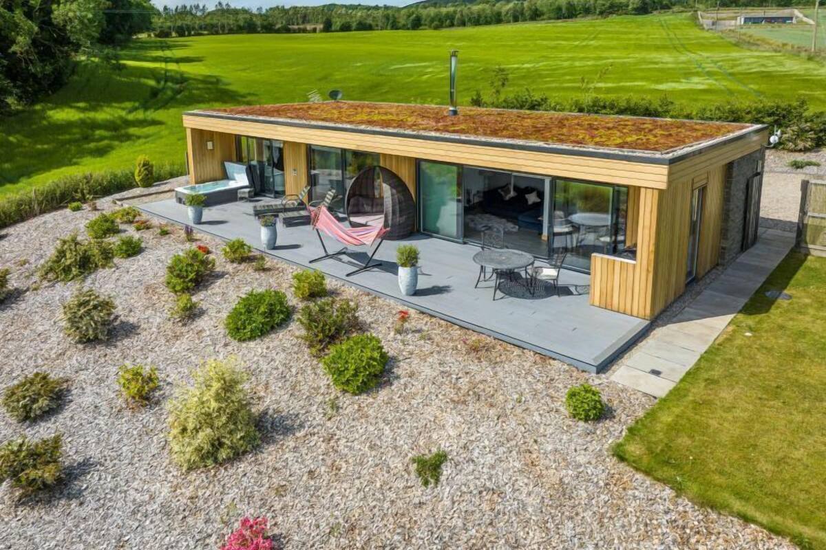 A modern house with a flat roof, large glass windows, and a patio area with outdoor furniture.