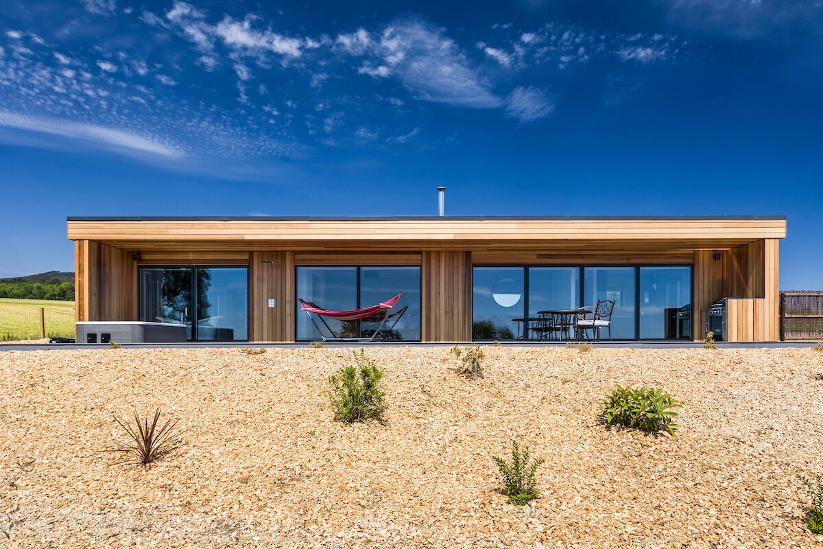 A modern building with large glass windows, a wooden exterior, and a gravel ground.