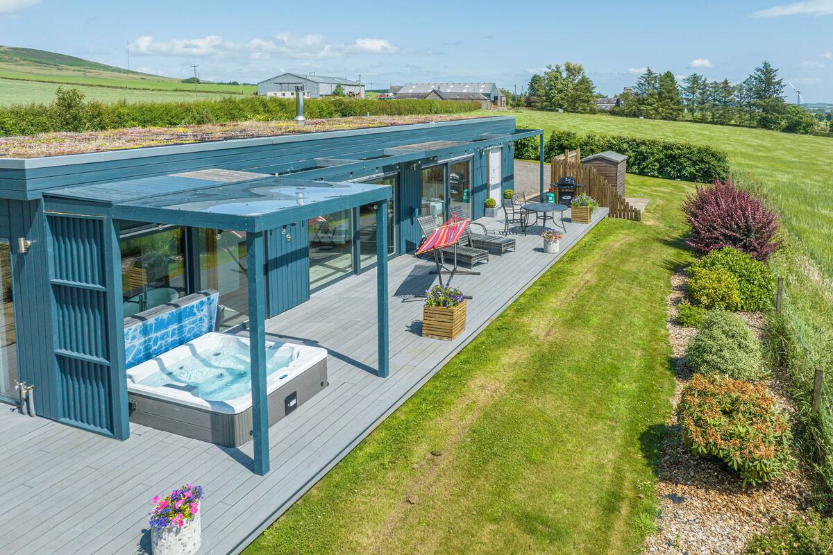 A modern outdoor deck with a hot tub, seating area, and a pergola.