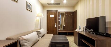 A hotel room with a sofa, a coffee table, a TV on a wooden stand, and a wardrobe.