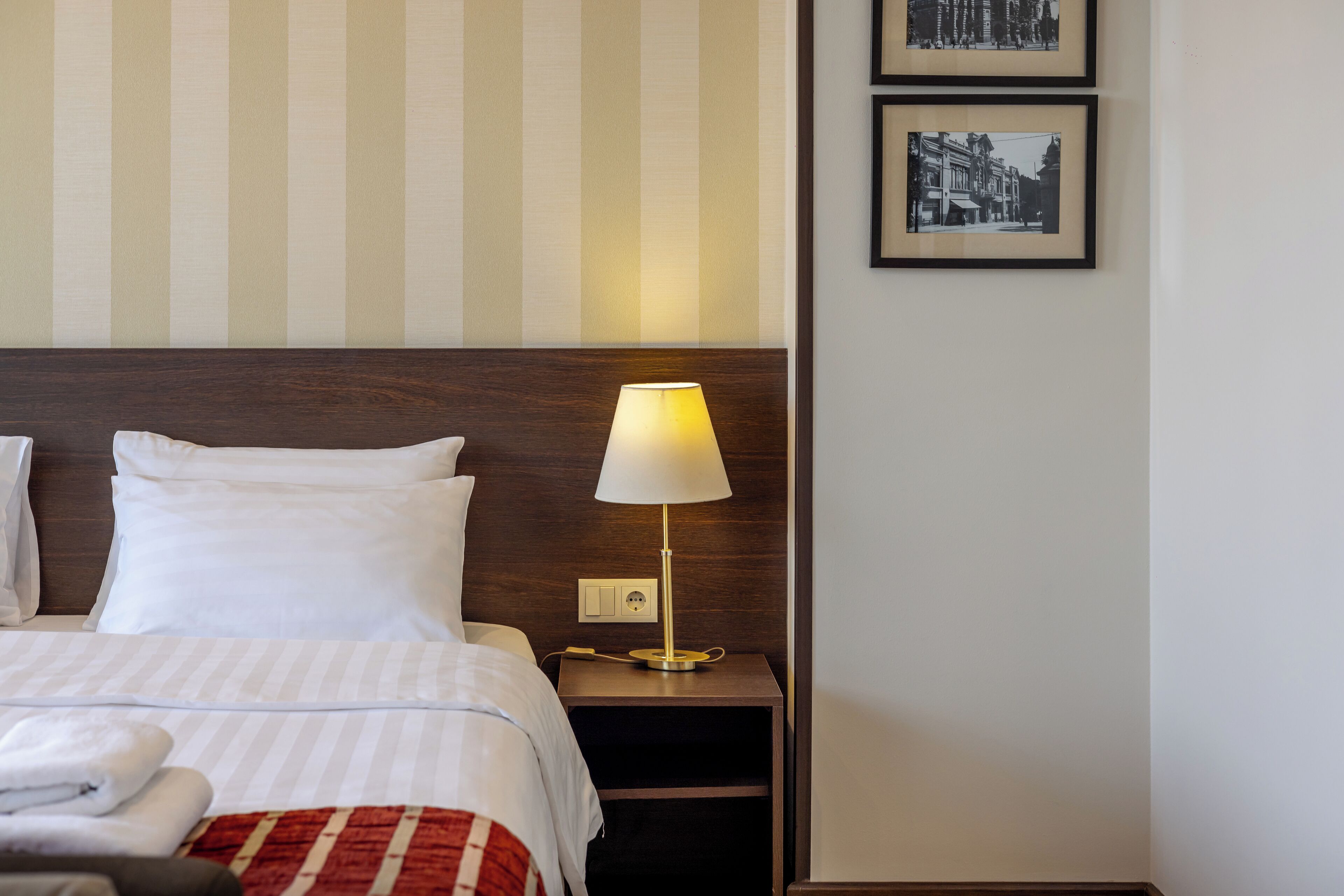 A neatly made bed with white bedding, a bedside lamp, and a nightstand with a power outlet.