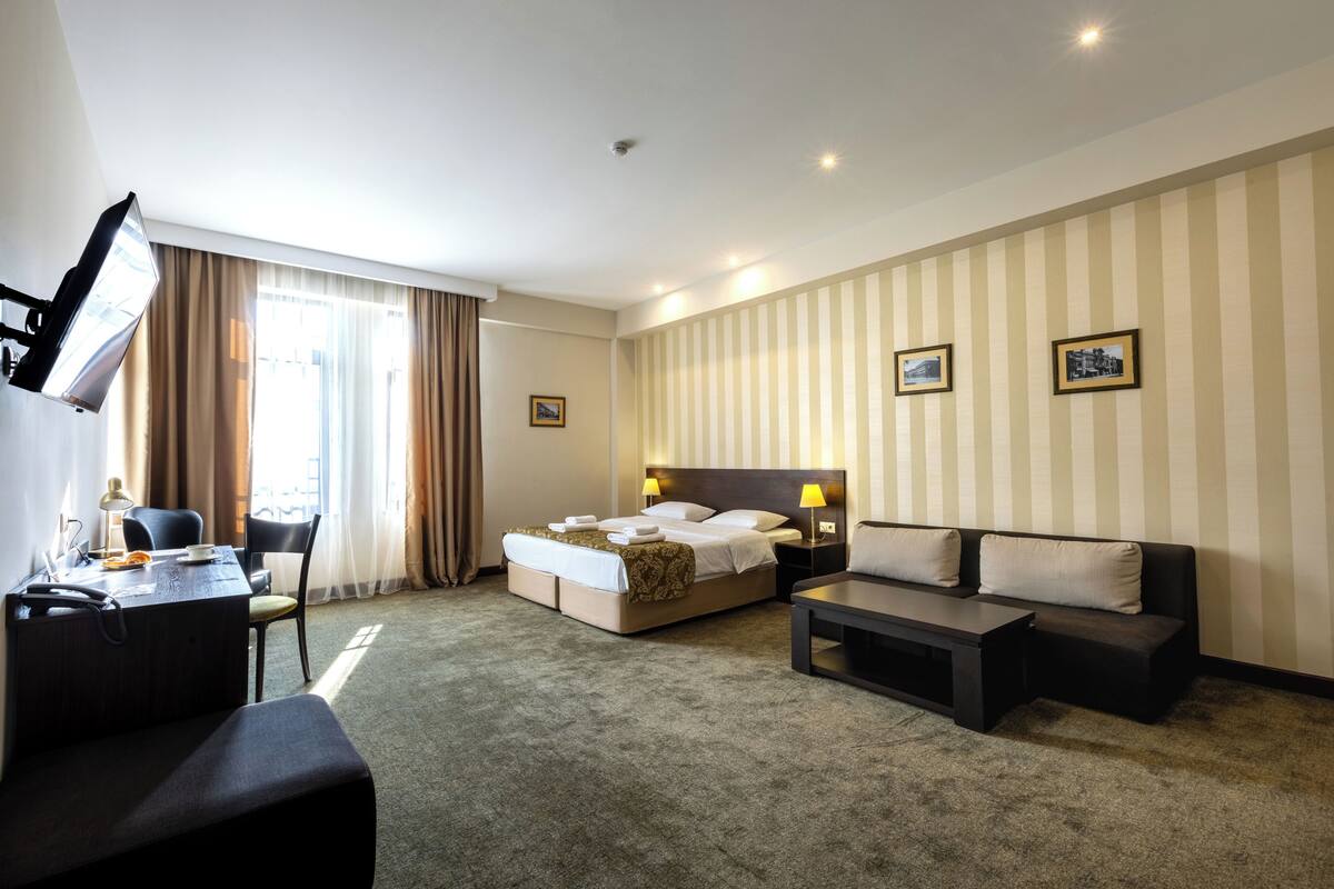 Habitación de hotel con cama, sofá, escritorio y una silla. Hay dos lámparas en la mesita de noche y un cuadro en la pared.