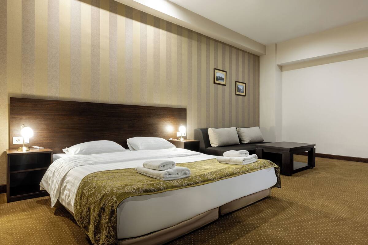 Una habitación de hotel con una cama grande, mesitas de noche, un sofá y una pequeña mesa.