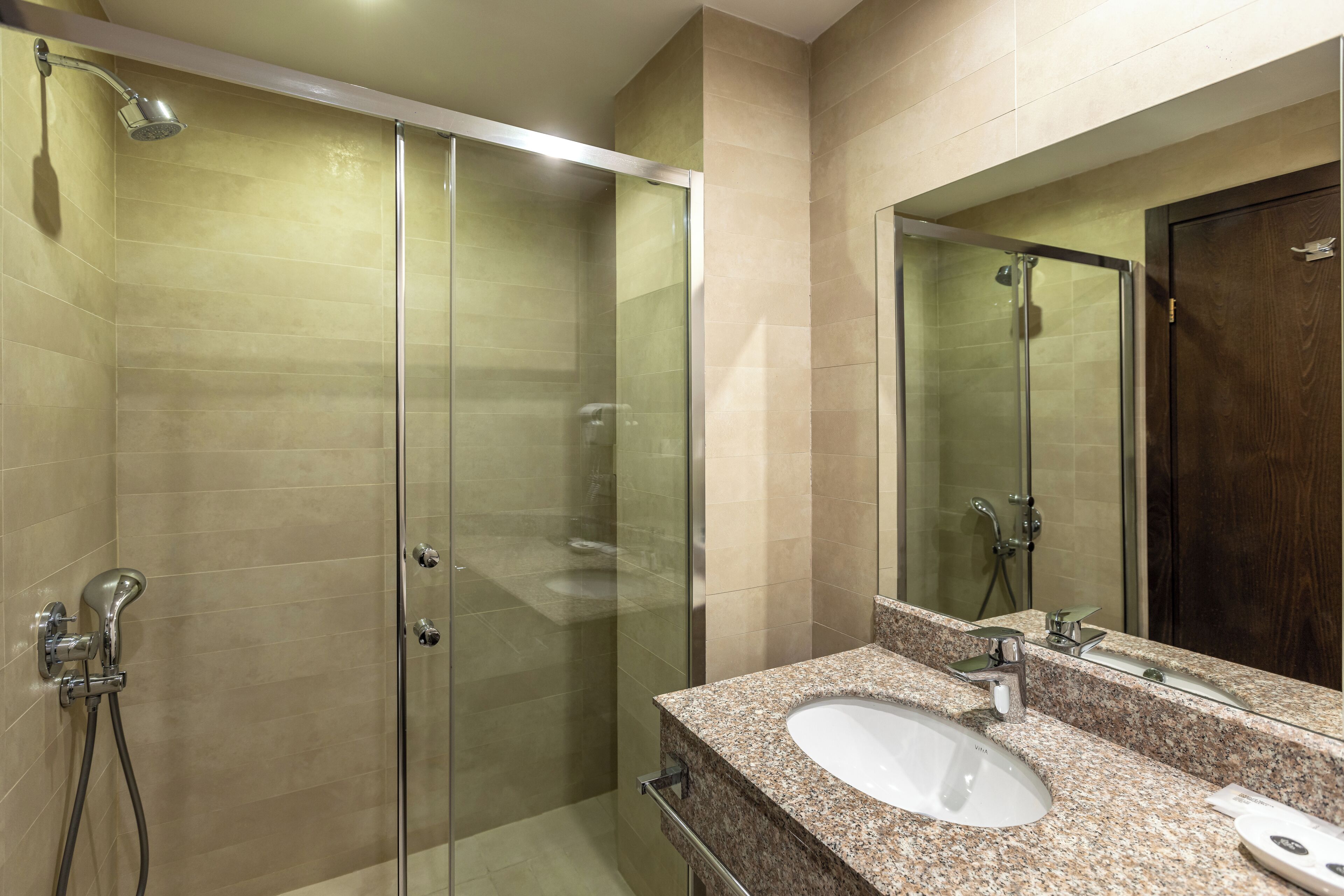 Een moderne badkamer met een douche met glazen wand, een granieten werkblad en een grote spiegel.