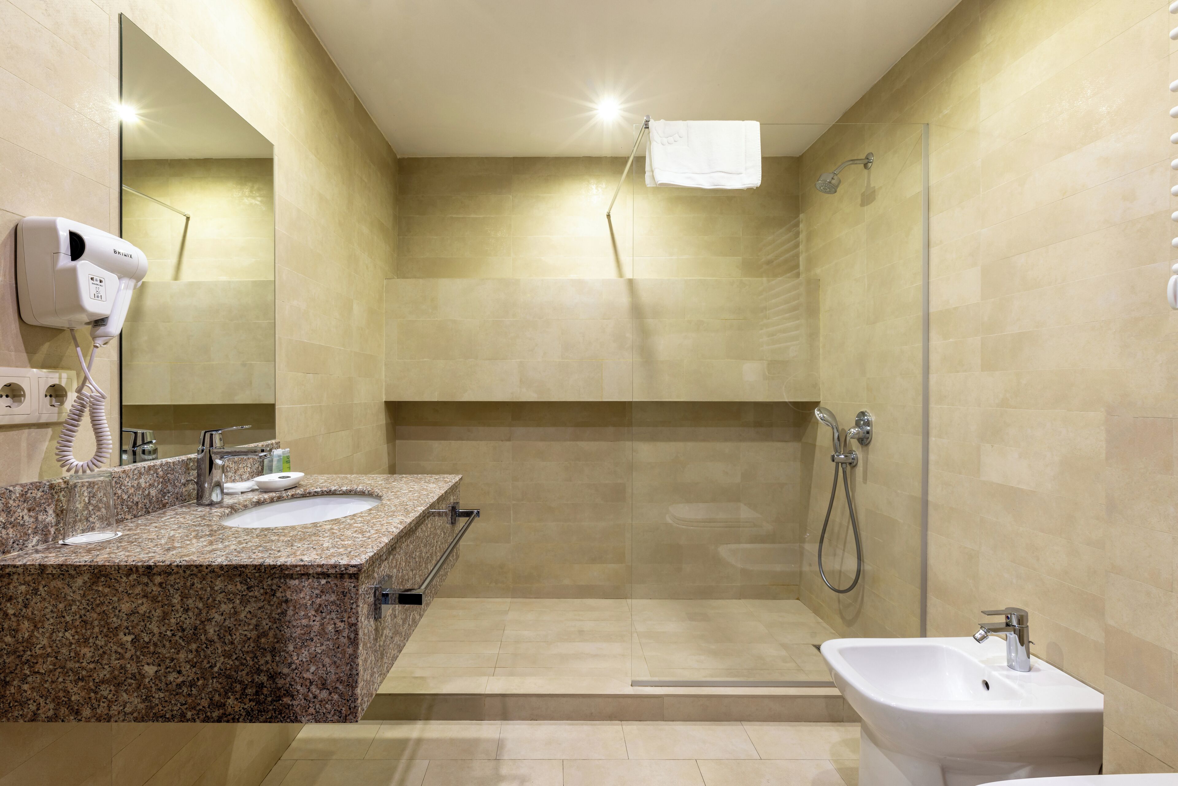 Un baño moderno con encimera de granito, lavabo, bidé y ducha.