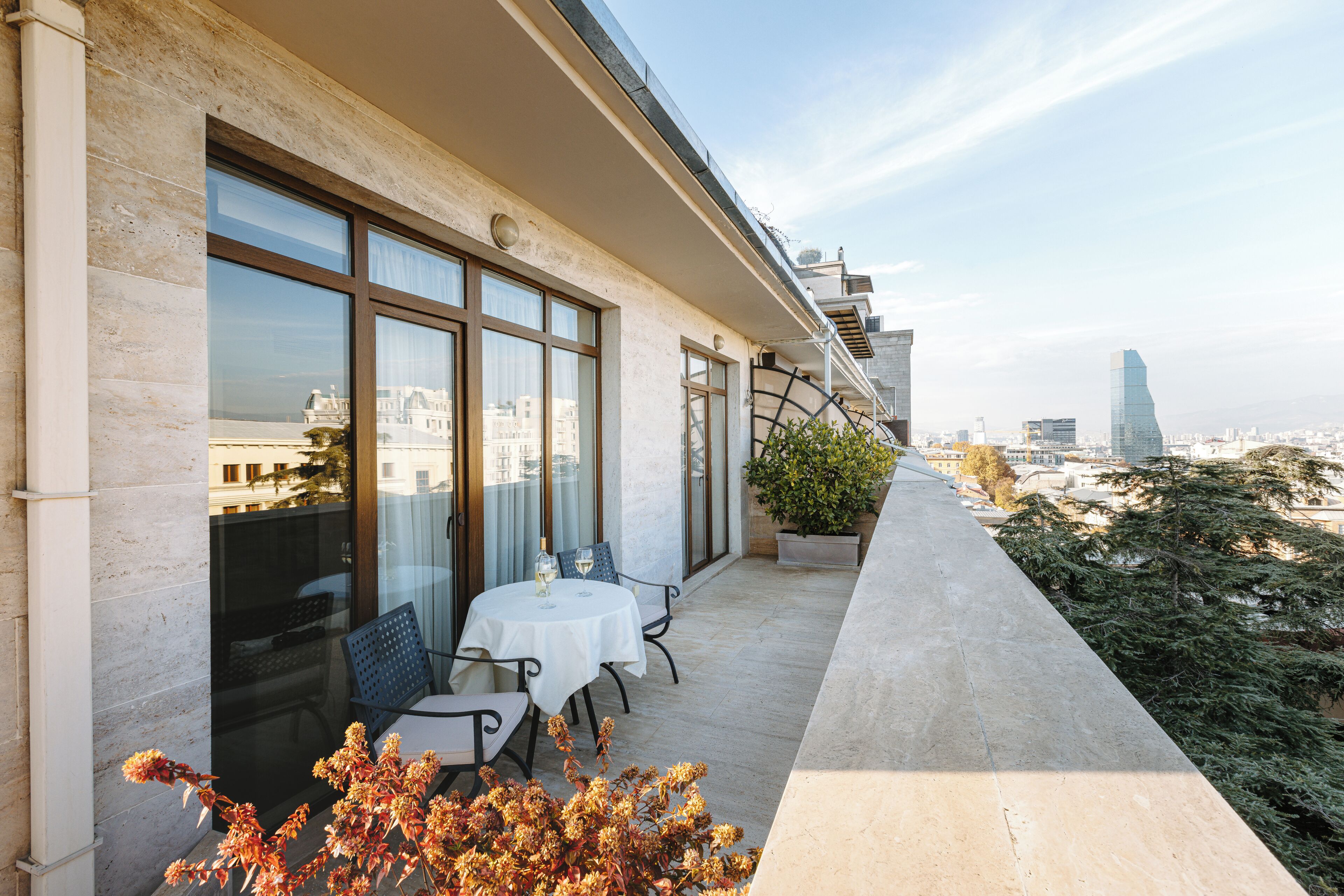 Un balcón con mesa y sillas, ventanas amplias y vistas panorámicas de la ciudad.