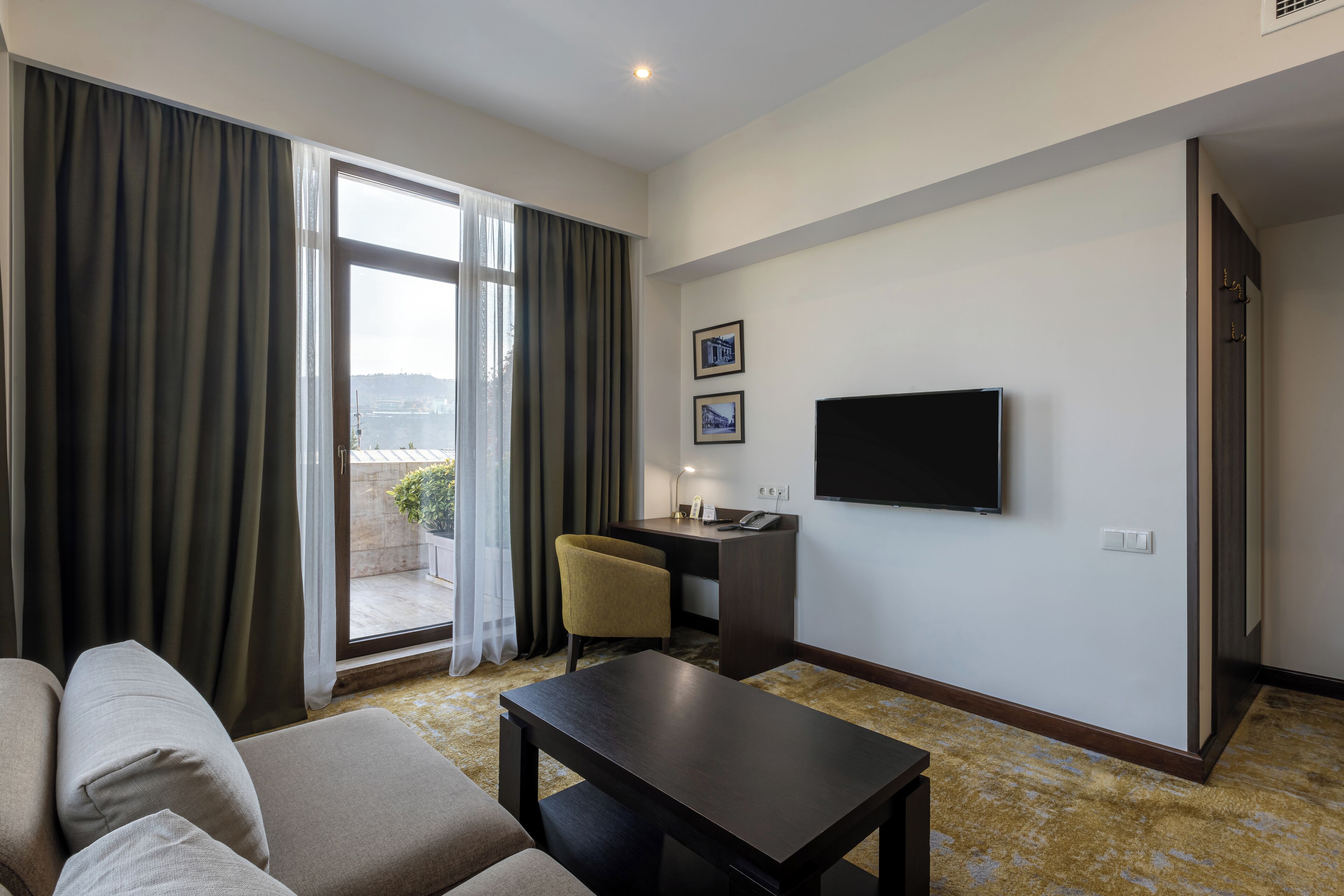A hotel room with a sofa, a desk, a television, and a view of the outdoors.