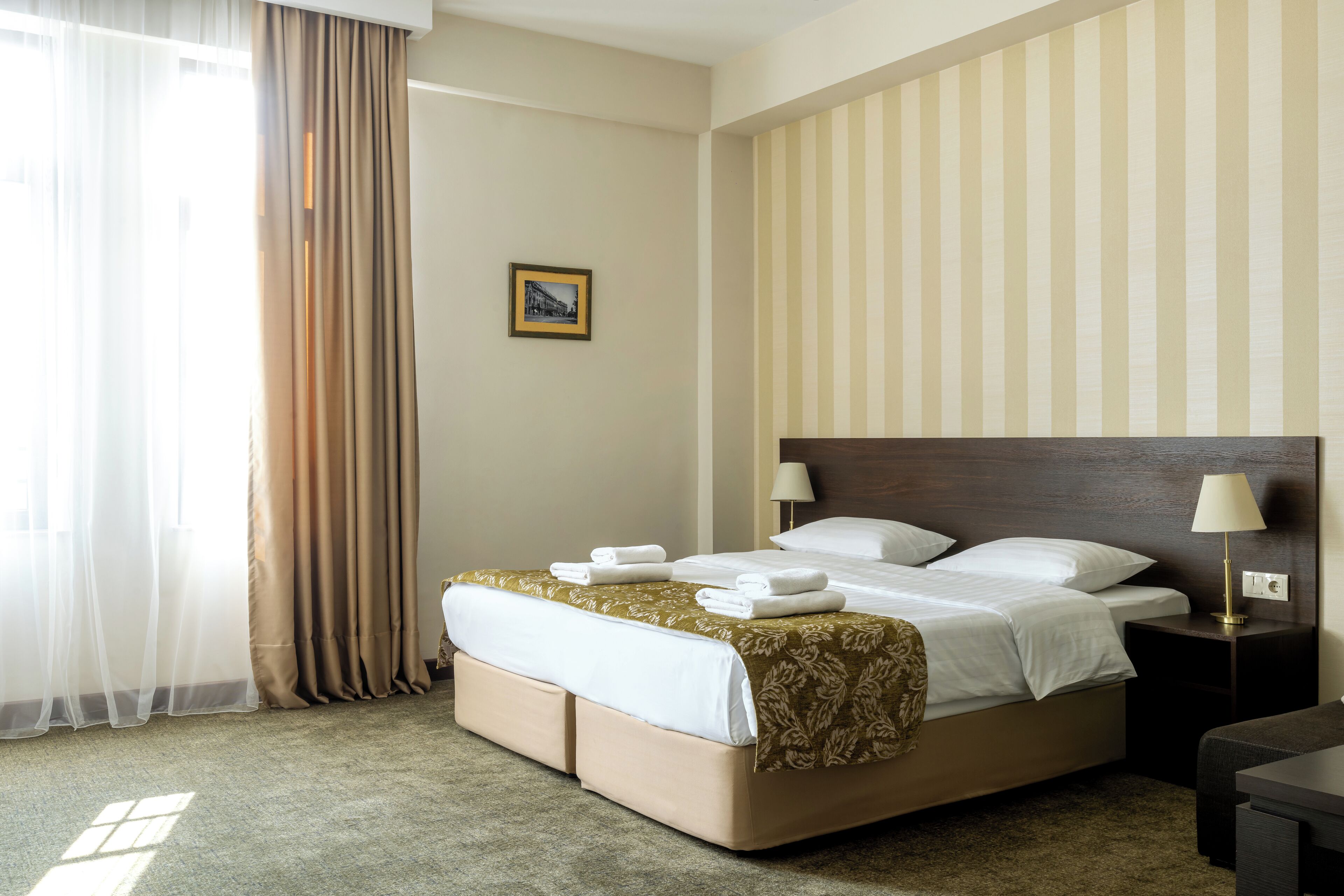 Une chambre d’hôtel avec un grand lit, une table de chevet avec une lampe, un tableau au mur et une fenêtre avec des rideaux.