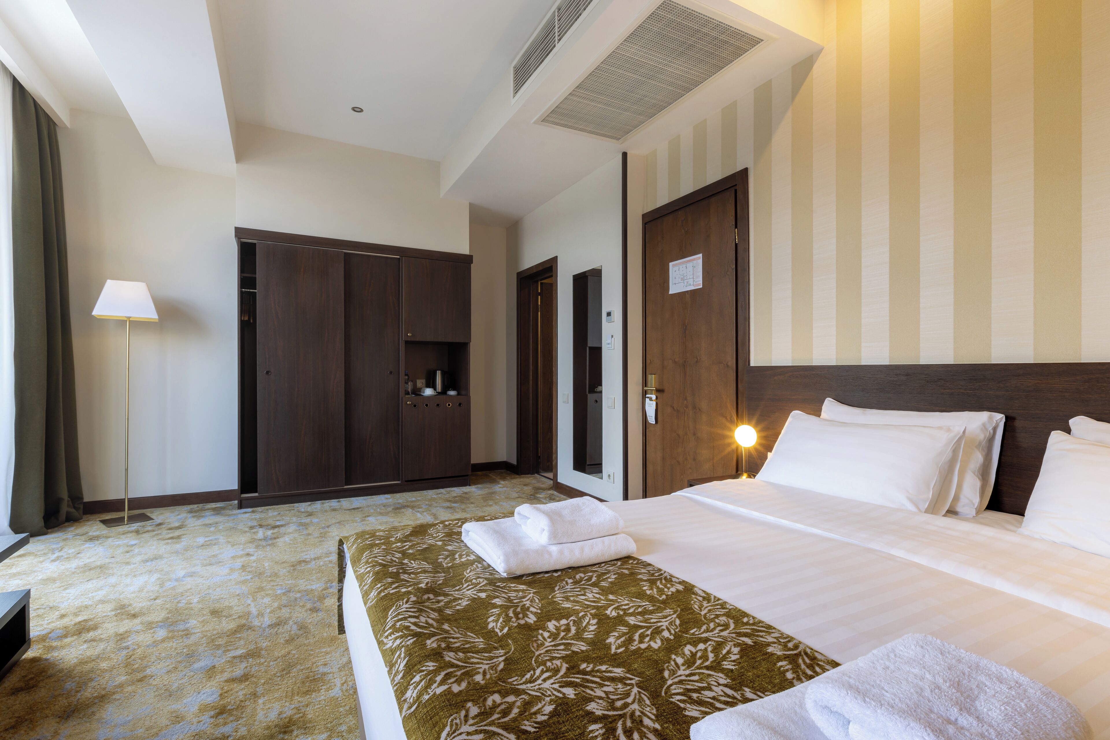 A hotel room with a large bed, a wardrobe, a desk, and a lamp.