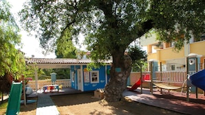 A playground with a slide, swings, and a small building with a red roof. - Club Anastasia Hotel (Marmaris)