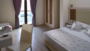 A hotel room with a bed, a desk with a chair, a wardrobe, and a view through the curtains. - Club Anastasia Hotel (Marmaris)