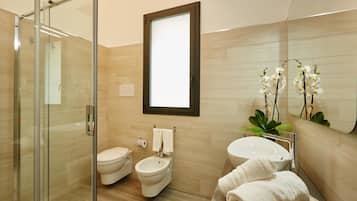 A modern bathroom with a glass shower enclosure, a toilet, bidet, and a sink with a mirror above.
