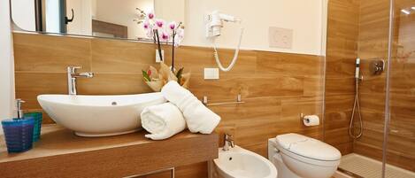 A modern bathroom with a large white sink, a bidet, a toilet, and a glass-enclosed shower.