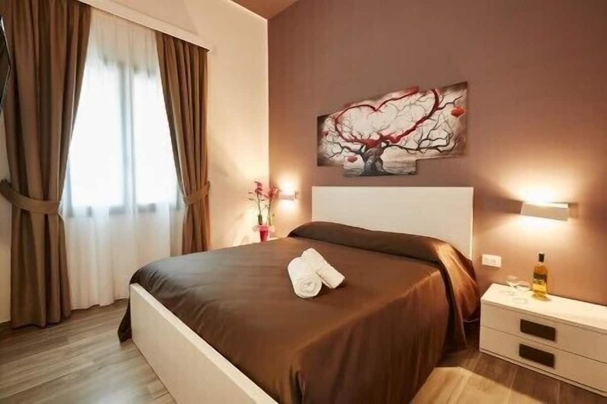 A hotel room with a bed, a nightstand, a lamp, and a painting on the wall.