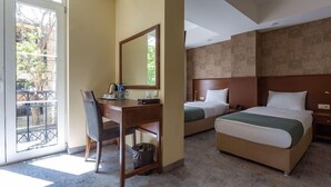 Una habitación de hotel con escritorio, dos camas, un espejo grande y vistas al exterior.