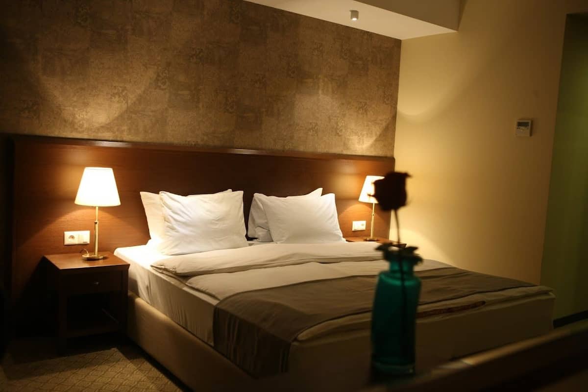 Une chambre d’hôtel avec un grand lit, deux lampes de chevet, une table de chevet et une bouteille posée sur le lit.