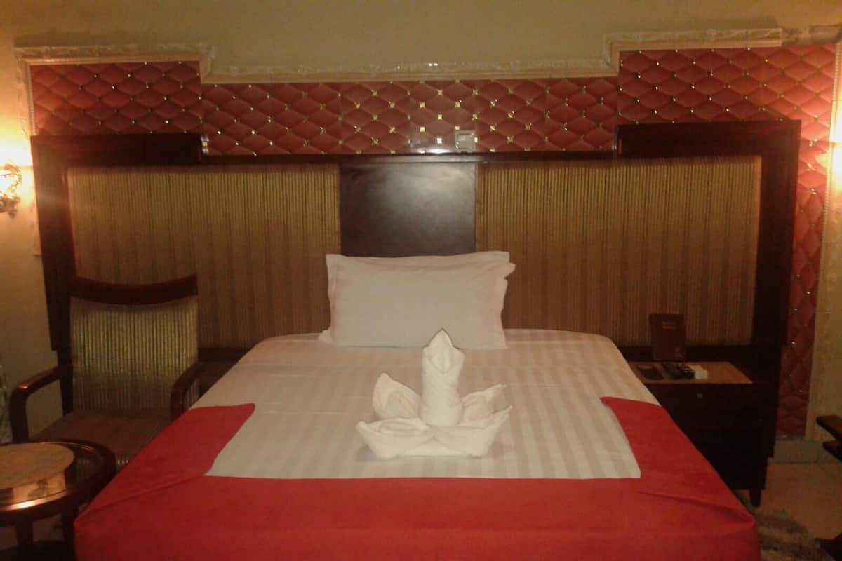 Habitación de hotel con una cama grande, un cabecero con diseño de rombos, una almohada decorativa roja y una toalla blanca sobre la cama.